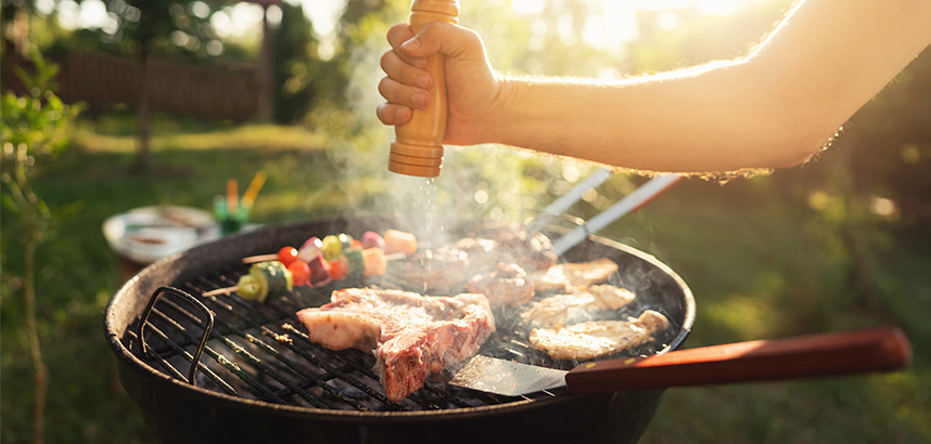 Person würzt Grillfleisch und Gemüse bei Sonnenuntergang im Garten.