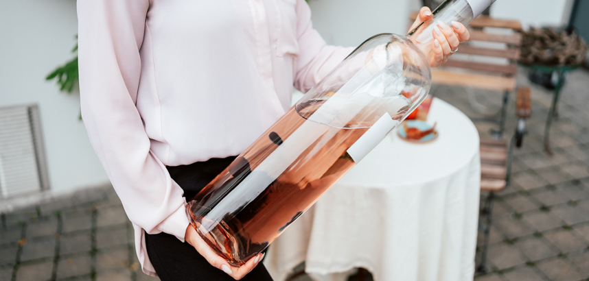 Person hält riesige Flasche Roséwein im Außenbereich nahe Tisch.