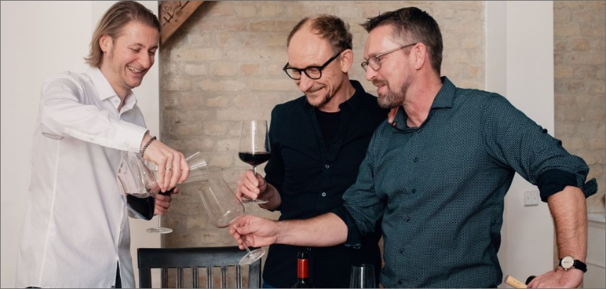 VINOS-Weinentdecker stoßen mit Weingläsern an, lächeln und unterhalten sich.